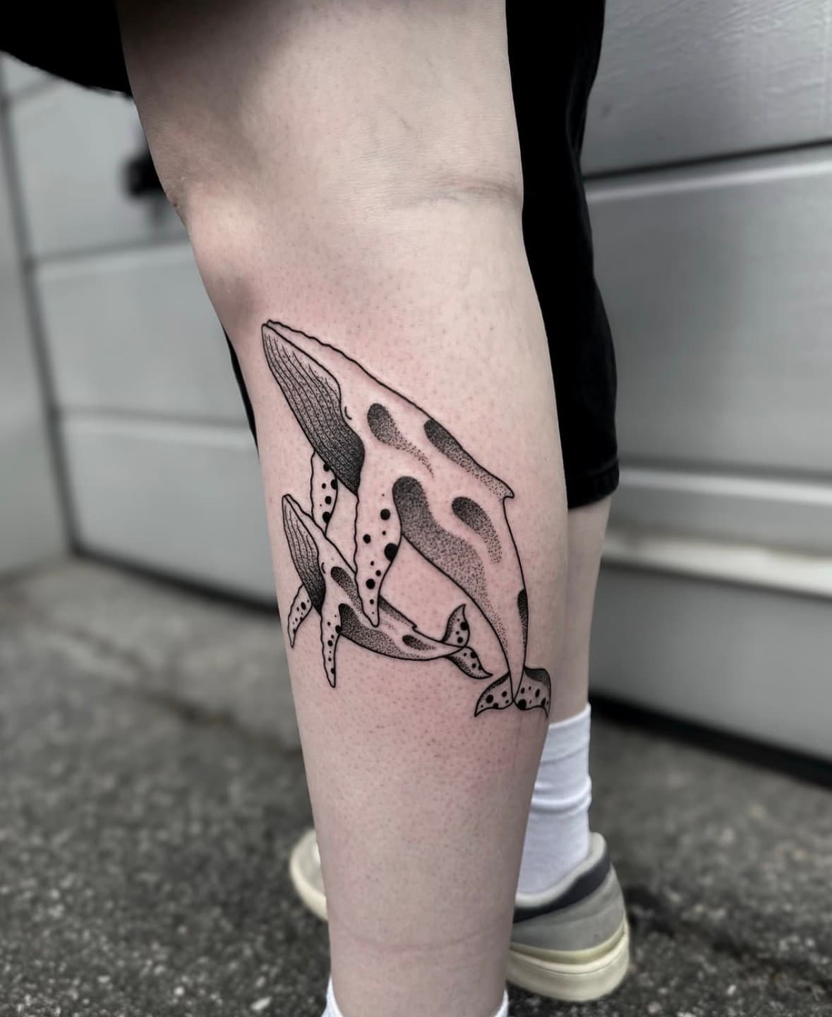 A tattoo of two whales, one is bigger than the other, they have dot shading and bigger dots.
